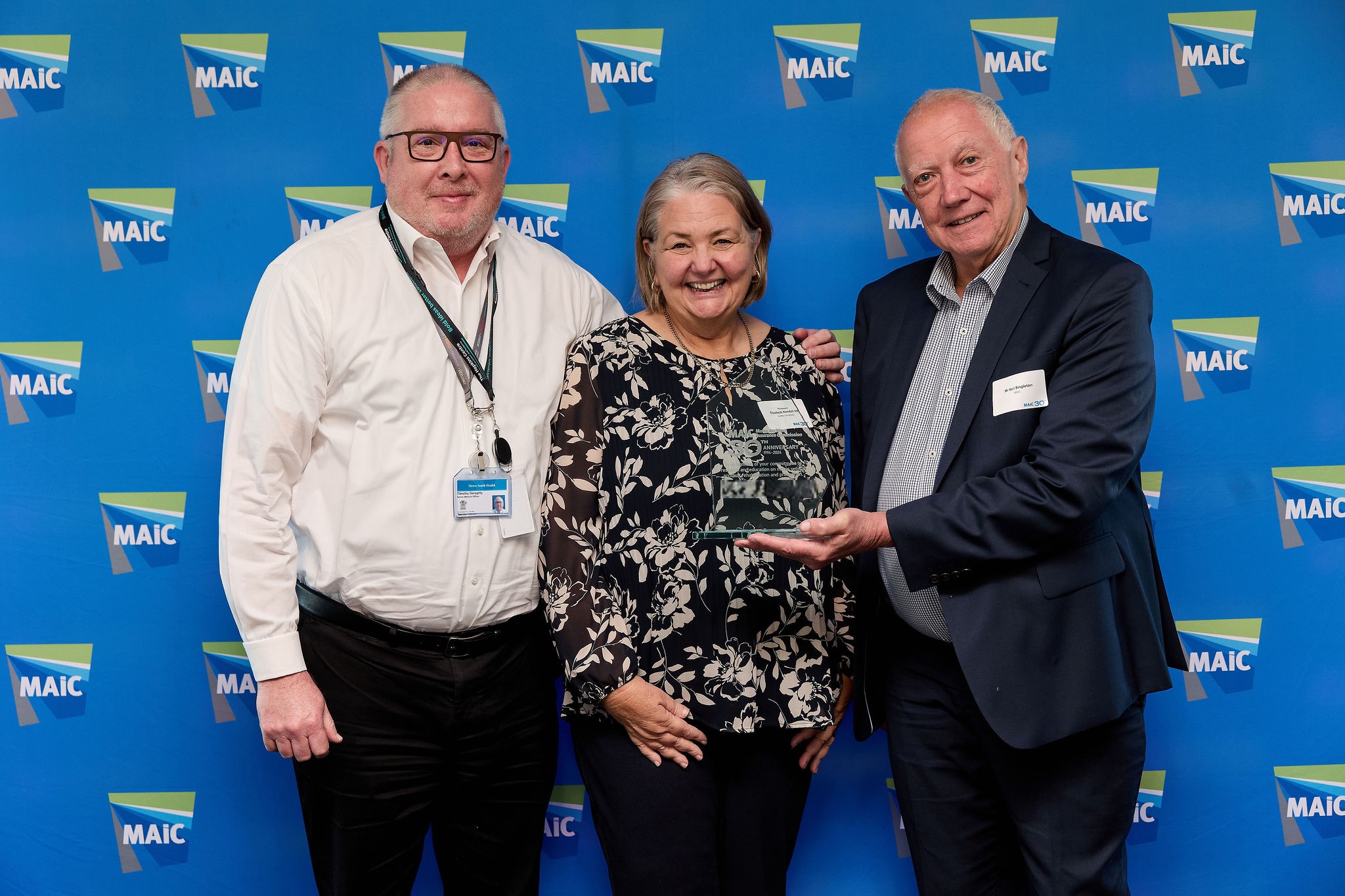 Professors Tim Geraghty and Elizabeth Kendall standing with a representative from MAIC, who is holding an award. 