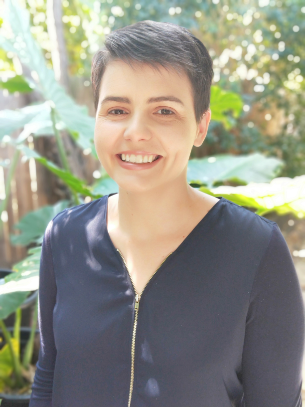 Profile image of Suzy Stoikov, a woman with short brown hair wearing a black shirt with a zip on the front. 